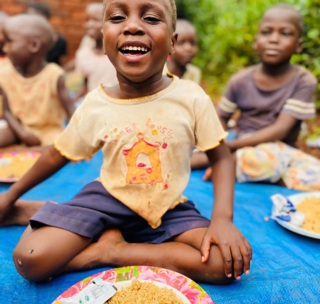 Smiling child sharing a meal at Kwaja Uganda